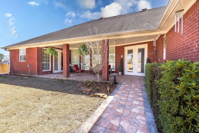 entrance to property featuring french doors, brick siding, and roof with shingles