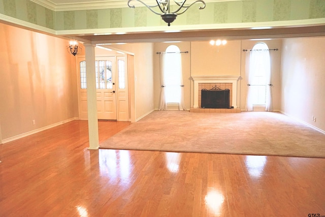 unfurnished living room featuring wood-type flooring, a notable chandelier, ornamental molding, and a tiled fireplace