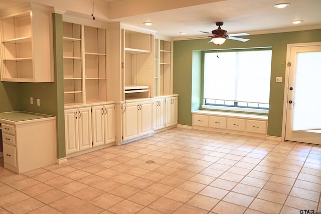 unfurnished living room featuring ceiling fan, light tile patterned floors, ornamental molding, and built in shelves