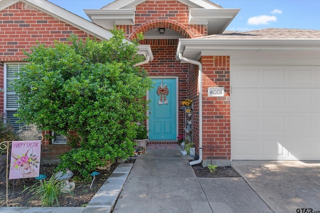 property entrance with a garage, concrete driveway, and brick siding