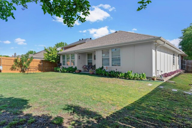 rear view of house featuring a lawn, a shingled roof, board and batten siding, and fence