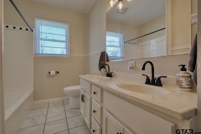 bathroom featuring toilet, double vanity, baseboards, and a sink