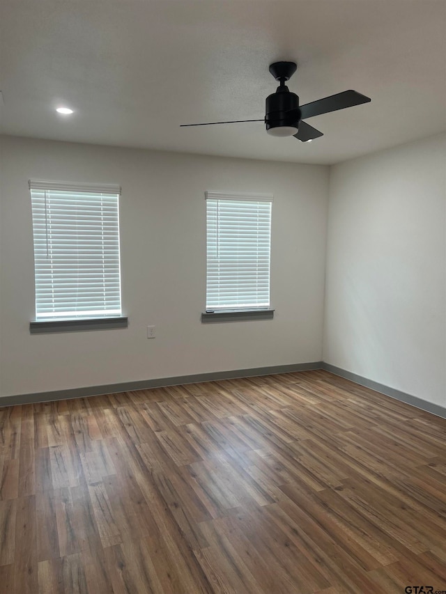 spare room with dark wood-type flooring, ceiling fan, and a healthy amount of sunlight