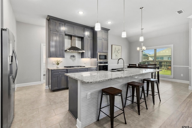 kitchen featuring sink, hanging light fixtures, wall chimney range hood, a kitchen island with sink, and appliances with stainless steel finishes