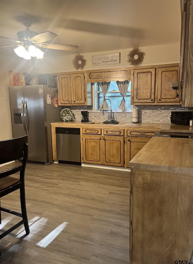 kitchen with decorative backsplash, light wood-style floors, appliances with stainless steel finishes, ceiling fan, and a sink