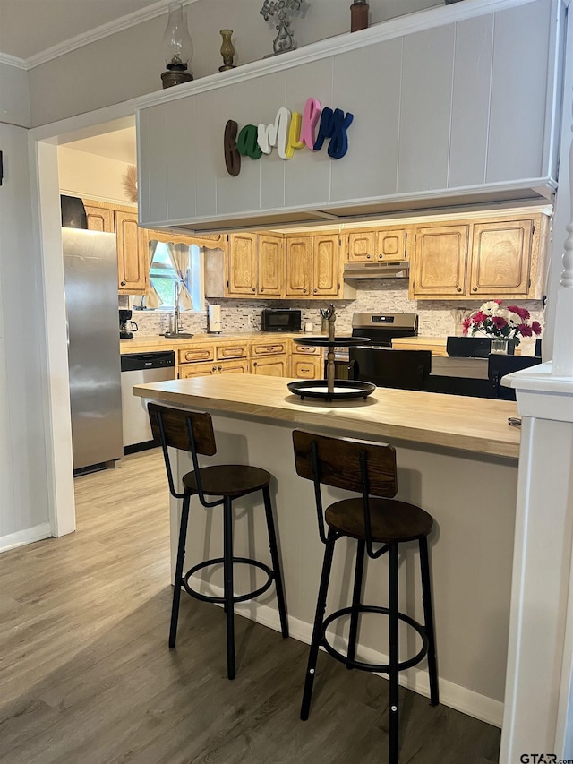 kitchen featuring ornamental molding, light wood finished floors, appliances with stainless steel finishes, and under cabinet range hood