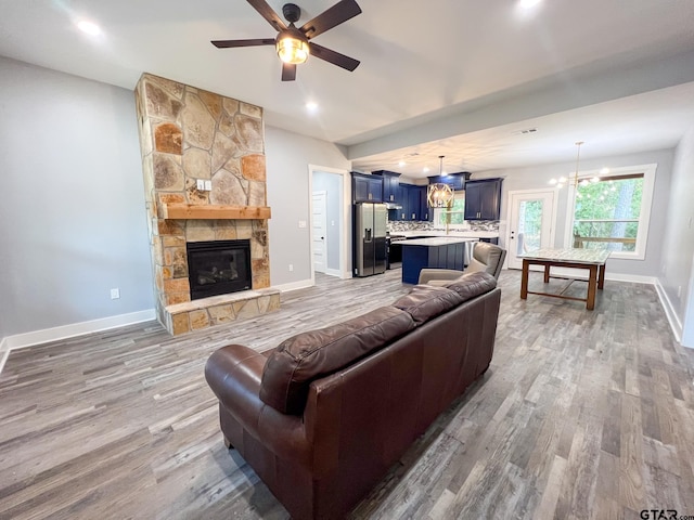 living room with a stone fireplace, hardwood / wood-style flooring, and ceiling fan with notable chandelier