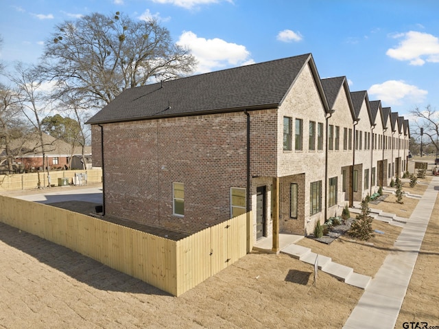 view of home's exterior with brick siding, fence, and a shingled roof