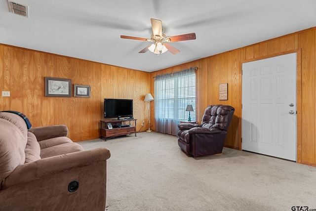 carpeted living room with ceiling fan, a textured ceiling, and wooden walls