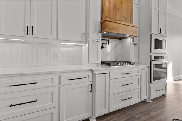 kitchen with white cabinetry, dark hardwood / wood-style flooring, stainless steel appliances, light stone countertops, and backsplash