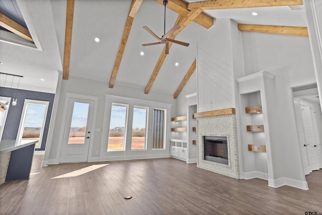 unfurnished living room featuring built in features, high vaulted ceiling, beamed ceiling, a brick fireplace, and a healthy amount of sunlight