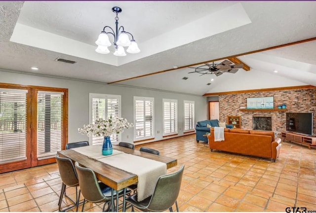 dining room featuring vaulted ceiling with beams, ceiling fan with notable chandelier, a textured ceiling, and a brick fireplace