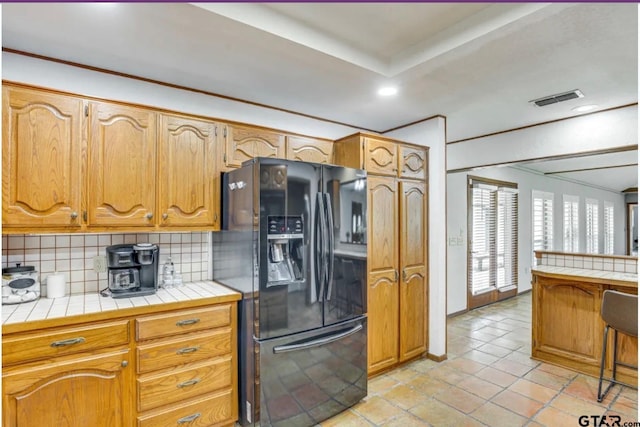 kitchen featuring tasteful backsplash, tile counters, black fridge with ice dispenser, and light tile patterned floors