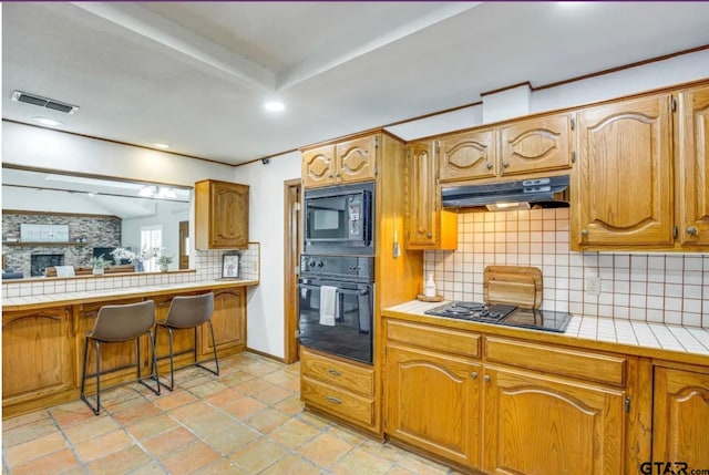 kitchen with a breakfast bar area, tile counters, decorative backsplash, and black appliances