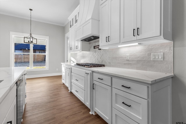 kitchen with pendant lighting, light stone countertops, white cabinetry, and ornamental molding