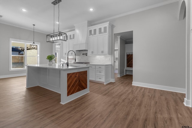 kitchen with white cabinets, custom range hood, a center island with sink, and ornamental molding