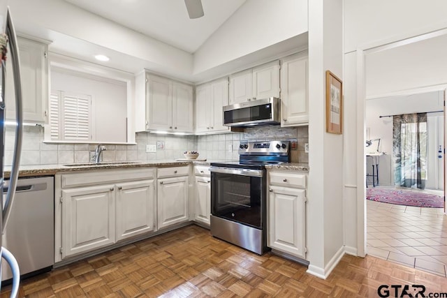 kitchen featuring lofted ceiling, a sink, white cabinets, appliances with stainless steel finishes, and backsplash