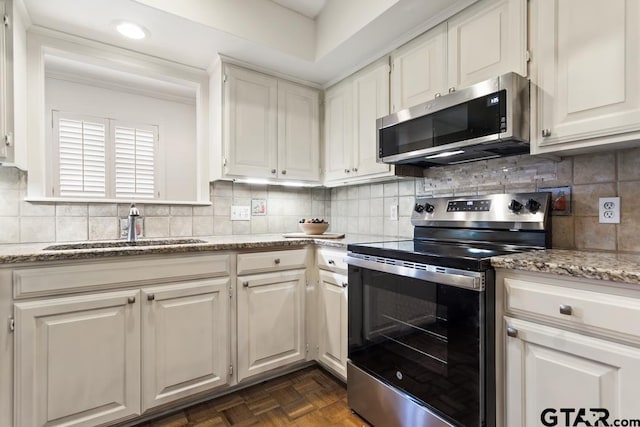 kitchen featuring appliances with stainless steel finishes, white cabinets, a sink, and tasteful backsplash