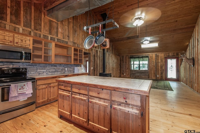 kitchen with a wood stove, lofted ceiling, appliances with stainless steel finishes, tile counters, and light hardwood / wood-style floors