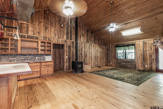 interior space featuring a wood stove, high vaulted ceiling, wood walls, wood ceiling, and light wood-type flooring