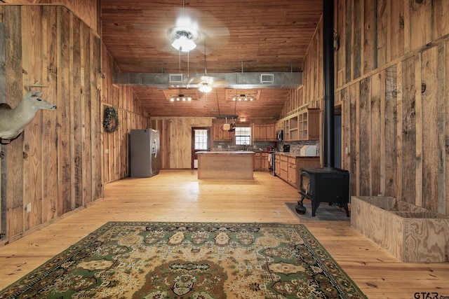 kitchen featuring light hardwood / wood-style floors, wood walls, a wood stove, and stainless steel appliances