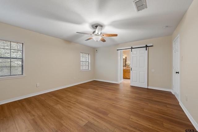 411 Raton, Holly Lake Ranch, TX 75765 - unfurnished bedroom featuring a barn door, wood finished floors, baseboards, a ceiling fan, and ensuite bathroom