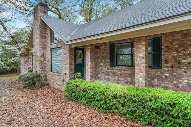 411 Raton, Holly Lake Ranch, TX 75765 - view of exterior entry featuring a shingled roof, a chimney, brick siding, and a porch