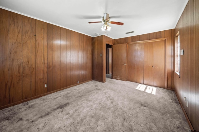 unfurnished bedroom featuring a closet, carpet floors, wood walls, visible vents, and ceiling fan