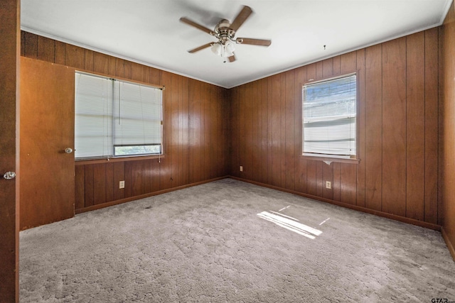 carpeted spare room with baseboards, wood walls, a healthy amount of sunlight, and a ceiling fan