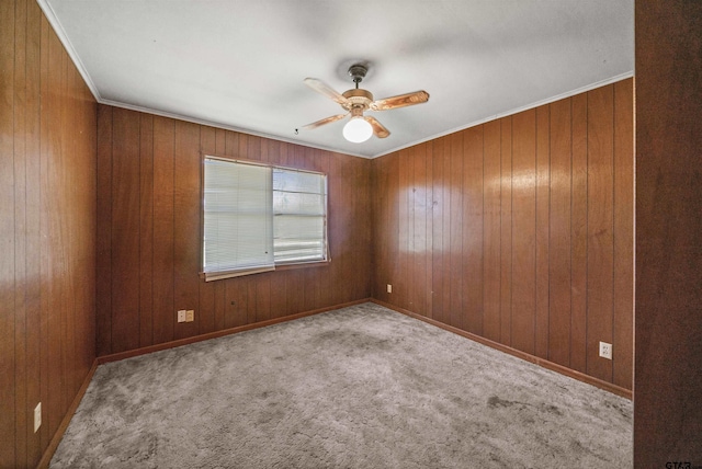 spare room featuring carpet flooring, wooden walls, baseboards, ceiling fan, and ornamental molding