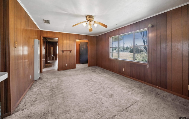 unfurnished bedroom featuring visible vents, wood walls, crown molding, a ceiling fan, and carpet floors