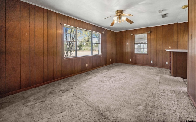 spare room featuring crown molding, wood walls, carpet flooring, and a ceiling fan