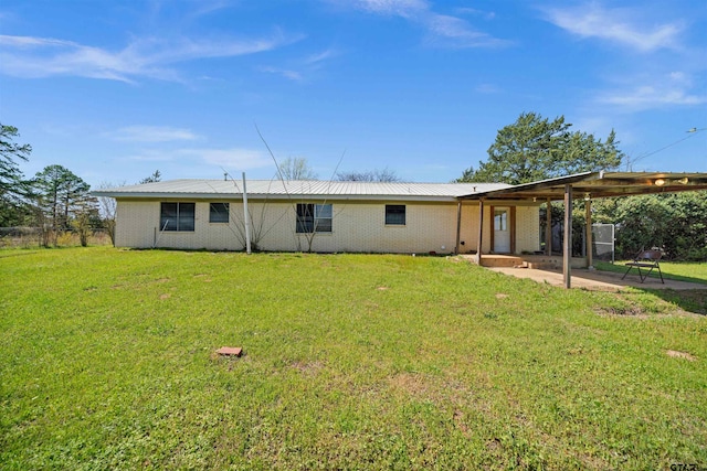 back of property with a lawn, metal roof, brick siding, and a patio area