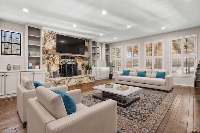 living room with built in shelves, a stone fireplace, and hardwood / wood-style floors