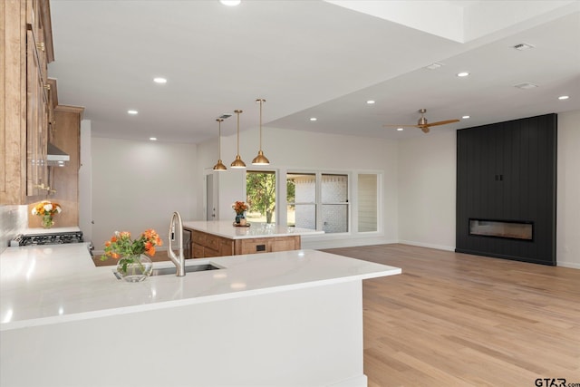 kitchen with light hardwood / wood-style floors, sink, a fireplace, a kitchen island, and pendant lighting