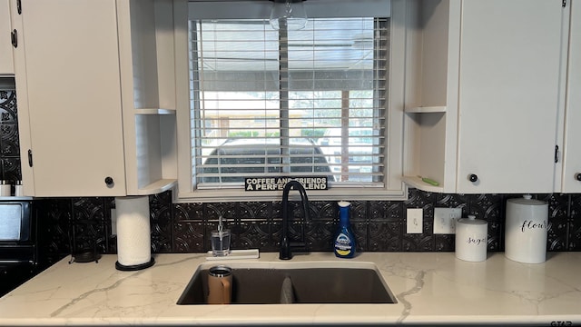 kitchen featuring tasteful backsplash, white cabinetry, a sink, and light stone countertops