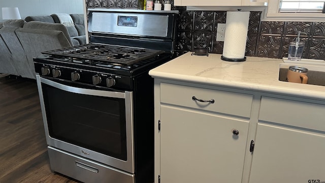 kitchen with stainless steel gas range, white cabinetry, decorative backsplash, and dark wood-type flooring