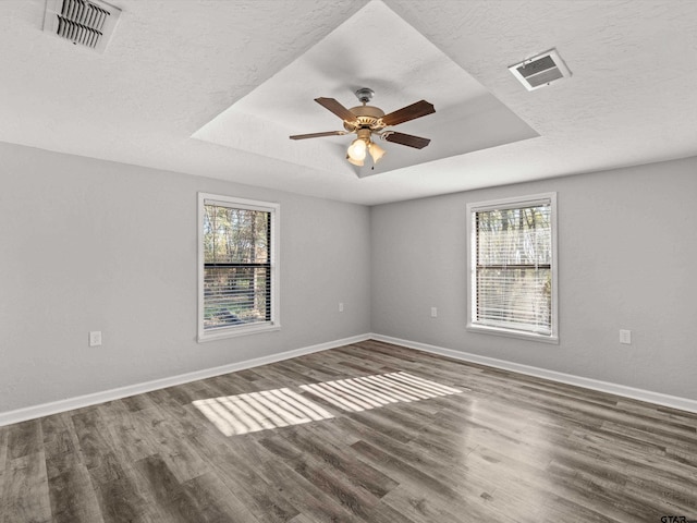 spare room featuring plenty of natural light, ceiling fan, dark hardwood / wood-style flooring, and a tray ceiling