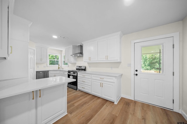 912 S Palmer Ave, Tyler, TX 75701 - kitchen with stainless steel appliances, wall chimney range hood, white cabinetry, light countertops, and light wood-style floors
