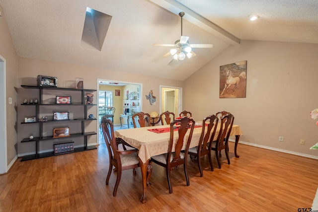 dining space with vaulted ceiling with beams, light wood-type flooring, baseboards, and a textured ceiling