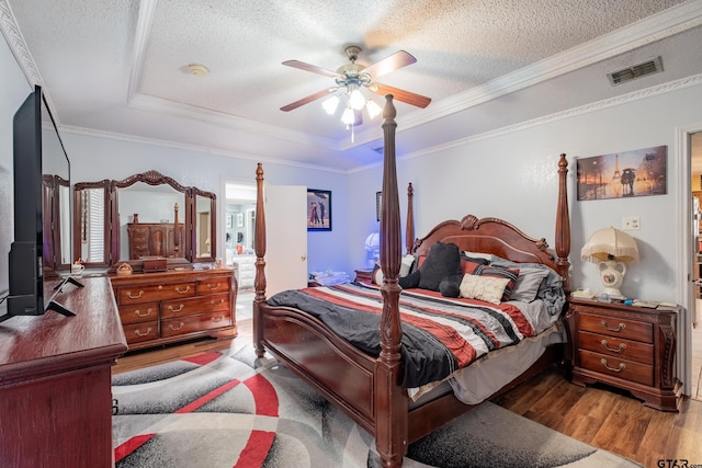 bedroom with visible vents, a raised ceiling, wood finished floors, crown molding, and a textured ceiling