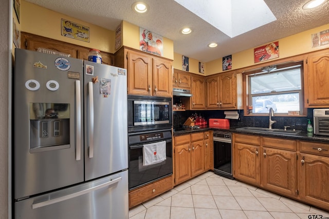 kitchen with stainless steel appliances, brown cabinetry, a skylight, and a sink