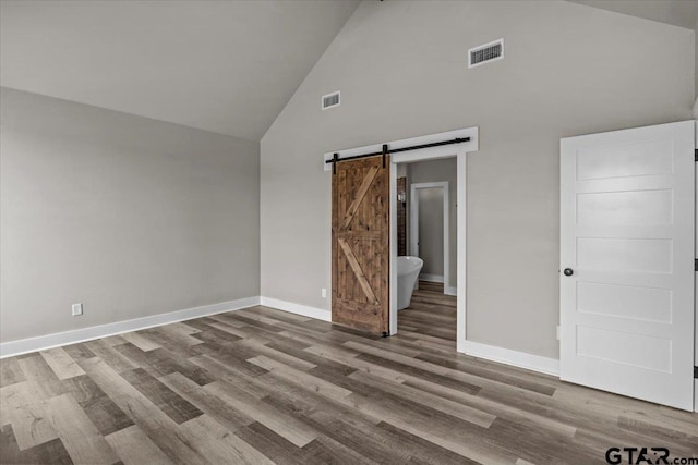 interior space featuring high vaulted ceiling, wood-type flooring, and a barn door