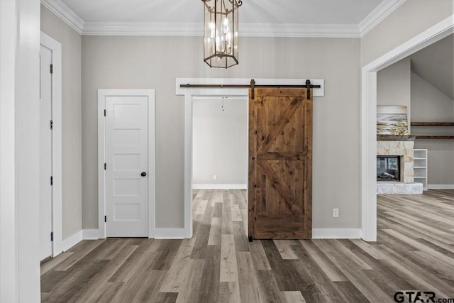 interior space with a fireplace, crown molding, a barn door, a notable chandelier, and hardwood / wood-style floors