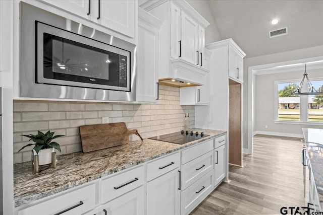 kitchen with black electric stovetop, stainless steel microwave, light stone countertops, white cabinetry, and light hardwood / wood-style flooring