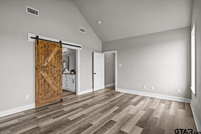 unfurnished bedroom featuring high vaulted ceiling, wood-type flooring, a barn door, and ensuite bath