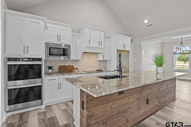 kitchen featuring white cabinets, an inviting chandelier, a center island with sink, and stainless steel appliances