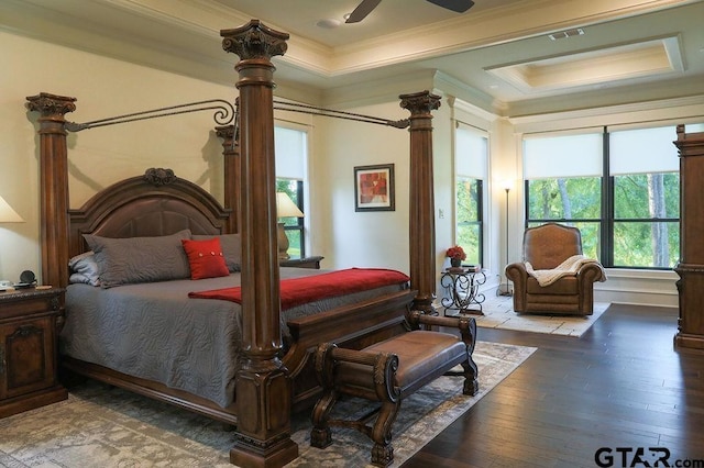 bedroom with ornamental molding, a raised ceiling, hardwood / wood-style flooring, ceiling fan, and decorative columns