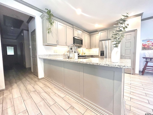 kitchen with light stone counters, stainless steel appliances, kitchen peninsula, and gray cabinetry