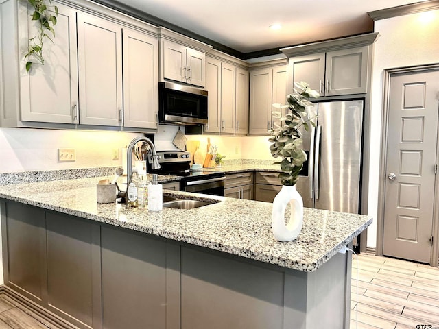 kitchen featuring sink, gray cabinets, appliances with stainless steel finishes, light stone countertops, and kitchen peninsula